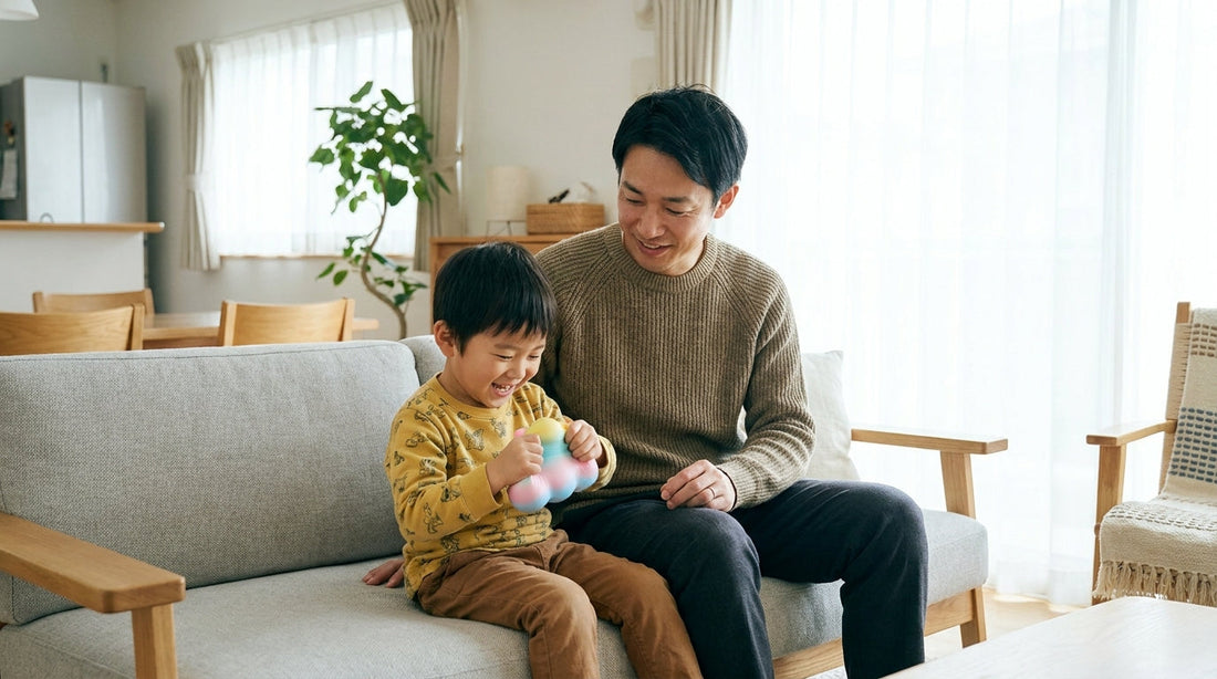 リビングのソファで、やわらかいボールを両手で持つ男の子と、となりで見守る大人の男性