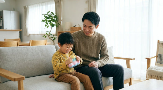 リビングのソファで、やわらかいボールを両手で持つ男の子と、となりで見守る大人の男性