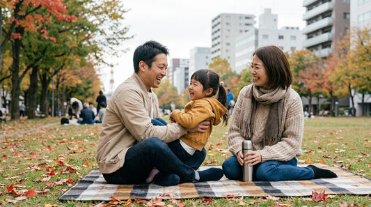 公園のレジャーシートで、女の子と大人の男性・女性が笑い合っている様子