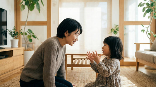 リビングで、両手を広げて話す小さな女の子と目線の高さを合わせて床に座り、笑顔で耳を傾ける大人の女性